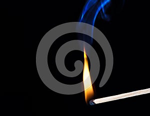 Burning wooden match with smoke over black background