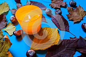 Burning yellow candle surrounded by autumn leaves and chestnuts lying on vivid blue background. Stylish autumn top view. Hello