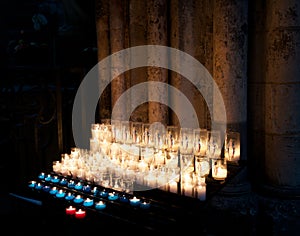 Burning yellow candles on a stand inside a church.  Burning candles in sconces on black blue background.