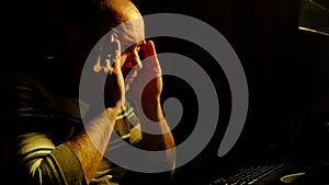 Burnout, fatigue concept. A man wearily rubs his temples in front of a computer at home at night