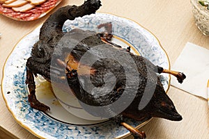 Burnt bird carcass on serving plate on dining table. Serve charred spoiled dish. Lousy housewife and bad chef. Overcook