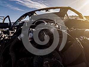 A burnt car engine with propeller after a fire or an accident in a parking lot covered with rust and black coal with scattered