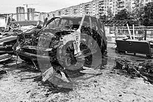 A burnt car after a fire or an accident in a parking lot covered with rust and black coal with scattered spare parts around.