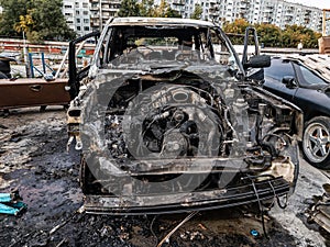 A burnt car after a fire or an accident in a parking lot covered with rust and black coal with scattered spare parts around.