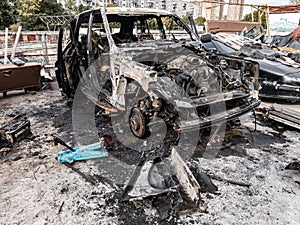 A burnt car after a fire or an accident in a parking lot covered with rust and black coal with scattered spare parts around.