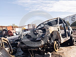 A burnt car after a fire or an accident in a parking lot covered with rust and black coal with scattered spare parts around.