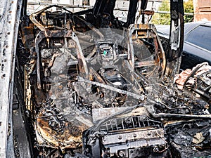 A burnt car interior after a fire or an accident in a parking lot covered with rust and black coal with scattered spare parts