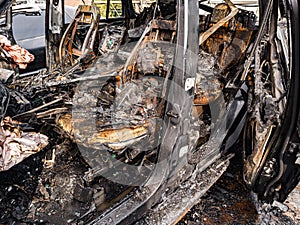A burnt car interior after a fire or an accident in a parking lot covered with rust and black coal with scattered spare parts