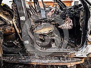 A burnt car interior after a fire or an accident in a parking lot covered with rust and black coal with scattered spare parts