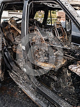 A burnt car interior after a fire or an accident in a parking lot covered with rust and black coal with scattered spare parts