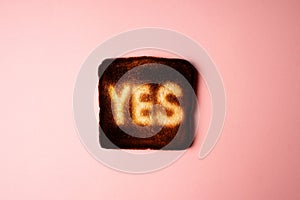 burnt dark slice of white bread toast with the word Yes on it on pink background