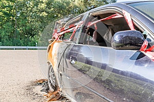 Burnt out car after a violent accident with police barrier tape in red and white with the German word for police barricade, German