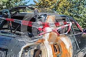 Burnt out car after a violent accident with police barrier tape in red and white with the German word for police barricade, German