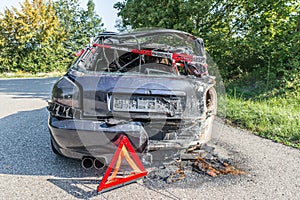 Burnt out car after a violent accident with police barrier tape in red and white with the German word for police barricade, German