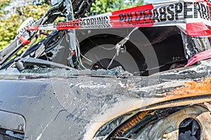 Burnt out car after a violent accident with police barrier tape in red and white with the German word for police barricade, German