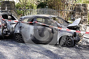 burnt out car wrecks behind police tape in residential street in Germany
