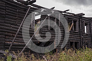 A burnt-out wooden log house against a dark gray sky. After the fire