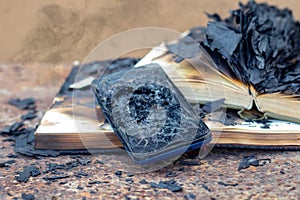 A burnt phone and burnt books in the smoke after a fire
