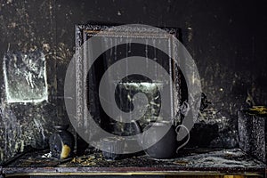 Burnt room interior. Burnt still life. Charred wall, picture frame, pot with burned rose in black soot