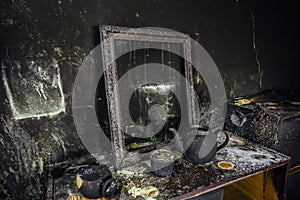 Burnt room interior. Burnt still life. Charred wall, picture frame, pot with burned rose in black soot