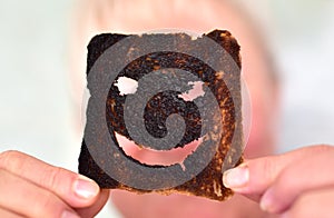 Burnt toast bread slices. Woman holds in hands a burnt slice of toast with an angry face expressing the emotion of sadness or