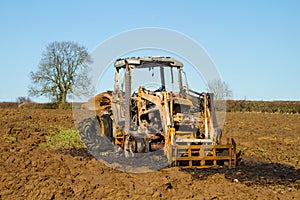 Burnt tractor digger in ploughed field