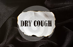 Burnt white piece of paper with text Dry Cough on a black fabric background