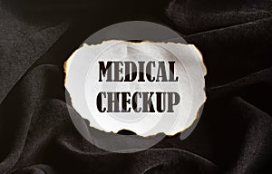 Burnt white piece of paper with text Medical Checkup on a black fabric background