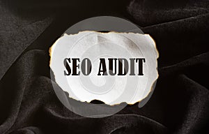 Burnt white piece of paper with text Seo Audit on a black fabric background