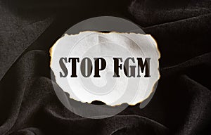 Burnt white piece of paper with text Stop Fgm on a black fabric background