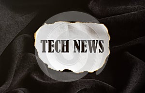 Burnt white piece of paper with text Tech News on a black fabric background