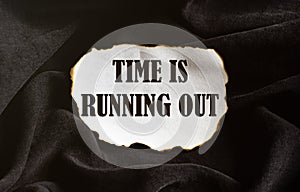 Burnt white piece of paper with text Time Is Running Out on a black fabric background