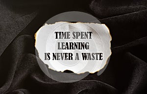 Burnt white piece of paper with text Time Spent Learning Is Never A Waste on a black fabric background