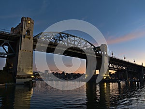 Burrard Street Bridge in the evening with illuminated pillars reflected in the water of False Creek bay in Vancouver, BC, Canada.