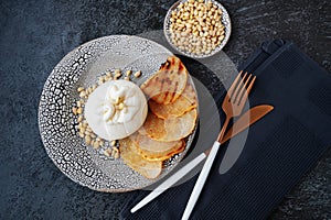 burrata with caramelized baked pear and pine nuts on a handmade clay plate . Top view, close-up