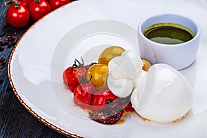 Burrata cheese with baked cherry tomatoes and pesto sauce on white plate