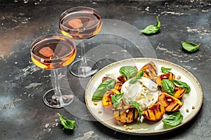Burrata cheese and grilled peaches with basil and pine nuts, Two glasses of rose wine on a dark background. Delicious antipasto.