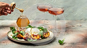 Burrata cheese and grilled peaches with basil and pine nuts, Two glasses of rose wine on a light background. Delicious antipasto.