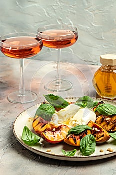 Burrata cheese and grilled peaches with basil and pine nuts, Two glasses of rose wine on a light background. Delicious antipasto.