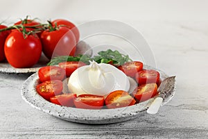 burrata with tomatoes. Caprese salad with tomatoes, burrata cheese and pine nuts. Cutaway soft cheese in a burrata bag