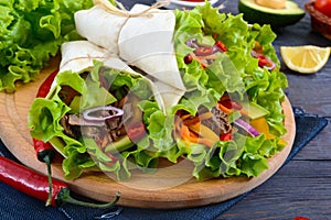 Burrito with chopped meat, avocado, vegetables, hot pepper on a cutting board on a dark wooden background.