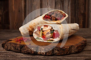 Burrito and shawarma wraps with beef and pork vegetables on wooden table. Copy space for text