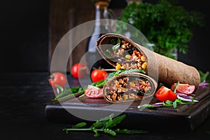 Burritos wraps with beef and vegetables on dark wooden background.