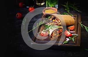 Burritos wraps with beef and vegetables on dark wooden background.