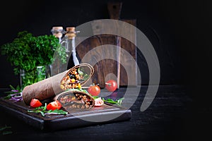 Burritos wraps with beef and vegetables on dark wooden background.