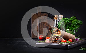 Burritos wraps with beef and vegetables on dark wooden background.