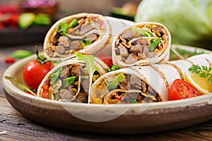 Burritos wraps with beef and vegetables on a wooden background.