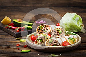 Burritos wraps with beef and vegetables on a wooden background.