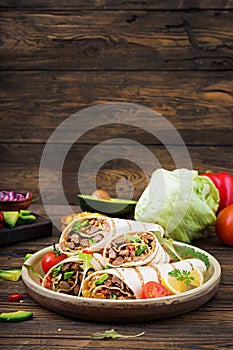 Burritos wraps with beef and vegetables on a wooden background
