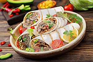 Burritos wraps with beef and vegetables on a wooden background.
